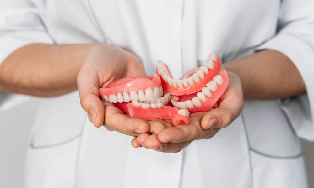 مقایسه ایمپلنت و دندان مصنوعی وقتی نوبت به جایگزینی دندان‌های از دست‌رفته می‌رسد، اغلب بیماران با یک دو راهی جدی روبه‌رو می‌شوند: ایمپلنت دندان یا دندان مصنوعی؟کدام روش ماندگاری بیشتری دارد؟ آیا می‌توان با اطمینان گفت ایمپلنت همیشه از پروتز دندانی دوام بالاتری دارد؟ از نظر زیبایی، راحتی و عملکرد در جویدن و صحبت کردن، کدام گزینه انتخاب هوشمندانه‌تری است؟این پرسش‌ها دغدغه مشترک بسیاری از افرادی است که به دنبال یک درمان مطمئن و ماندگار هستند؛ سوالاتی که اگر پاسخ دقیق و شفافی برای آن‌ها وجود نداشته باشد، تصمیم‌گیری را دشوار می‌کند. در ادامه، به‌طور کامل و واقع‌بینانه به مقایسه ایمپلنت دندان و دندان مصنوعی می‌پردازیم تا انتخابی آگاهانه‌تر داشته باشید. مقایسه ایمپلنت و دندان مصنوعی مزایا و معایب ایمپلنت دندان در مقایسه با دندان مصنوعی مزایای ایمپلنت دندان ایمپلنت دندان در مقایسه با پروتز دندانی دارای مزایای چشمگیری است که تجربه‌ای نزدیک به دندان طبیعی را برای بیمار فراهم می‌کند: ویژگی ایمپلنت دندان توضیح عملکرد جویدن عالی ایمپلنت به دلیل اتصال مستقیم به استخوان فک، فشارهای جویدن را به خوبی تحمل می‌کند و تجربه‌ای مشابه دندان طبیعی دارد. زیبایی طبیعی و جذاب تاج ایمپلنت می‌تواند دقیقاً شبیه دندان طبیعی ساخته شود و لثه نیز در لبخند حفظ می‌شود. سلامت استخوان پیشگیری از تحلیل استخوان ایمپلنت با تحریک استخوان فک، از تحلیل آن جلوگیری می‌کند و سلامت دهان را در بلندمدت حفظ می‌کند. دوام و استحکام بسیار بالا پایه تیتانیومی و تاج مقاوم ایمپلنت، طول عمر بالایی دارد و تقریباً درمانی دائمی محسوب می‌شود. مقایسه ایمپلنت و دندان مصنوعی ایمپلنت دندان بهتر است یا دندان مصنوعی اینکه کدام روش برای جایگزینی دندان‌های از دست‌رفته شما انتخاب بهتری است، پاسخ یکسانی برای همه ندارد و به مجموعه‌ای از عوامل مهم بستگی دارد. ایمپلنت دندان و دندان مصنوعی هر دو می‌توانند راه‌حل مناسبی برای درمان باشند، اما تفاوت‌های اساسی در جنس، عملکرد، میزان راحتی، دوام و حتی زیبایی ظاهری دارند. از سوی دیگر، هزینه درمان در این دو روش اختلاف قابل‌توجهی دارد و همین موضوع نقش مهمی در تصمیم‌گیری بیماران ایفا می‌کند.اگر می‌خواهید انتخابی آگاهانه و متناسب با شرایط دهان، سبک زندگی و بودجه خود داشته باشید، ابتدا باید با تفاوت‌ها، مزایا و محدودیت‌های هر یک آشنا شوید. شناخت دقیق این موارد به شما کمک می‌کند بهترین گزینه را برای بازگرداندن لبخند و عملکرد طبیعی دندان‌هایتان انتخاب کنید.